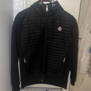 Svart quiltad pufferjacka Moncler XL - Svart pufferjacka från Moncler Grenoble i storlek XL. Jackan har quiltad framsida och rygg. Med luva