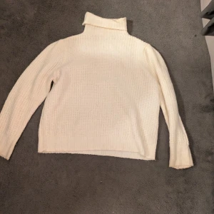 Vit stickad polotröja - Säljer en vit stickad polotröja med hög krage och långärmad design. Tröjan har en mjuk och grovstickad struktur.