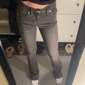 Grå bootcut jeans från True Religion - Snygga grå jeans från True Religion i modellen Becca (färg charcoal) med bootcut passform och mid waist. Jeansen har klassiska fem fickor, dekorativa sömmar och en ikonisk bakficka med knapp. Materialet är mjukt jeans-tyg med stretch för skön passform. Endast använda en gång. (Jag är 165)