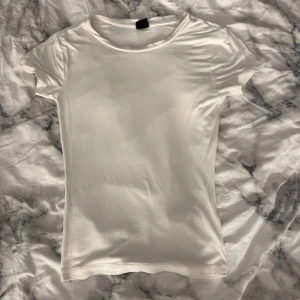 Vit basic t-shirt från Gina Tricot - En klassisk vit t-shirt från Gina Tricot i storlek XS. T-shirten har rund halsringning och korta ärmar, perfekt för en clean och enkel look. Tillverkad i mjukt material som känns skönt mot huden.