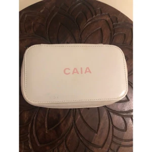 Vit necessär från CAIA med dragkedja - Snygg och stilren necessär från CAIA i vit färg med ljusrosa insida. Väskan har ett rektangulärt format och stängs med dragkedja runtom. Perfekt för smink eller småprylar, enkel att ta med i väskan. Sparsamt använd. Liten