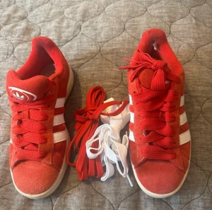 Röda Adidas Campus sneakers - Säljer ett par röda Adidas Campus sneakers med klassiska vita ränder på sidorna och vit logga på plösen. Skorna har rund tå, platt sula och är gjorda i mocka med snörning. Medföljer bara röda skosnören. Storlek 38! 