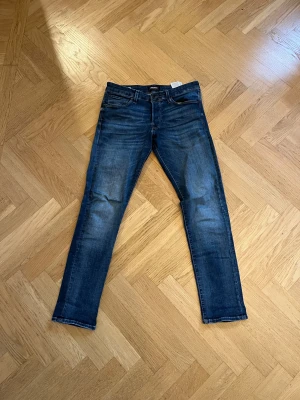 Blå slim jeans från Jack & Jones - Snygga blå jeans från Jack & Jones i modellen Glenn. De har en slim passform, klassisk femficksdesign och subtila slitningar för en cool look. Jeansen är tillverkade i stretchigt denim som sitter skönt hela dagen. Hör av er vid frågor
