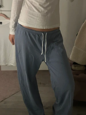 Blå mjukisbyxor från Brandy Melville - Säljer ett par chill blå mjukisbyxor från Brandy Melville med vit snörning i midjan. Byxorna har loose passform, låg midja och är gjorda i mjukt bomullsmaterial. Perfekta för att hänga hemma eller dra till kompisar i.