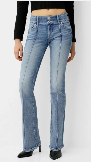 Blå bootcut jeans med låg midja - Snygga ljusblå jeans med bootcut passform och låg midja. Jeansen har klassisk femficksdesign, dubbla knappar i midjan och markerade sömmar längs benen. Perfekt för dig som gillar en retro vibe och vill ha ett par jeans som sitter tajt upptill och släpper vid vaden.
