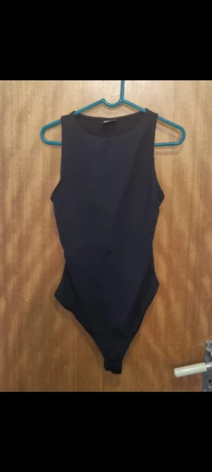 Svart ärmlös bodysuit - Säljer en stilren svart bodysuit med rund hals och ärmlös design. Toppen har en tight passform och är perfekt att matcha med jeans eller kjol. Materialet känns mjukt och stretchigt, vilket gör den bekväm att bära hela dagen.