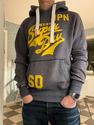 Superdry JPN hoodie - En sjukt snygg hoodie från Superdry med vintage stil. Riktigt snygg färgkombination som ögonen fäster sig vid🤩Storlek M. Riktigt bra passform och skönt tyg, passar personer med storlek S också(som mig), är 176cm lång. Är som nyskick förutom små sprickor i trycket som syns på bilderna😁Frårgor och prisförslag tas gärna med emot🙂Mvh