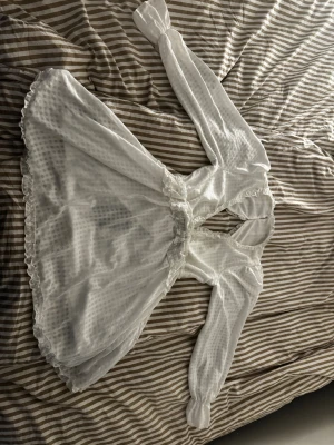 Studentklänning / Vit klänning - Superfin vit kortklänning från Dennis Maglic med långärmade puffärmar, volangdetaljer och öppen rygg. Klänningen har ett diskret rutigt mönster i tyget och knappar i nacken. Jätte gullig och passar som perfekt som studentklänning !! Storlek L och helt ny med prislappen på. Nypris 899 kr   Första 2 bilderna är framsidan, 3-5 är baksidan och sista bilden är bevis på att den ej är använd.   Länken till klänningen är https://dennismaglic.com/sv/products/veronica-dress  , så man kan se bättre bilder 