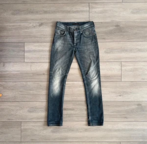 Blå jeans från Nudie Jeans, storlek 31/32 - Snygga blå jeans från Nudie Jeans med klassisk femficksdesign och coola slitningar på framsidan. Jeansen har en normal passform och är tillverkade i slitstarkt bomullsmaterial. Bakfickan har Nudie Jeans signaturbroderi och läderpatch med logga.