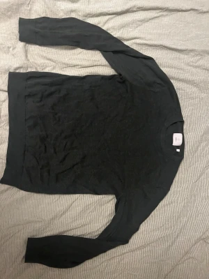 Mörkgrön stickad tröja från Bläck - En stilren svart stickad tröja från Bläck i storlek S. Tröjan har rund halsringning, ribbade muddar och långärmad design. Perfekt för dig som gillar enkel och clean look. Materialet är mjukt och passar bra till lager-på-lager under höst och vinter.