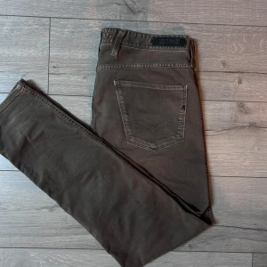 Beige jeans från Replay - Snygga bruna jeansbyxor från Replay i modellen Anbass. De har en klassisk femficksdesign och en knappgylf. Perfekta för en stilren look. Priset kan diskuteras vid snabb affär.