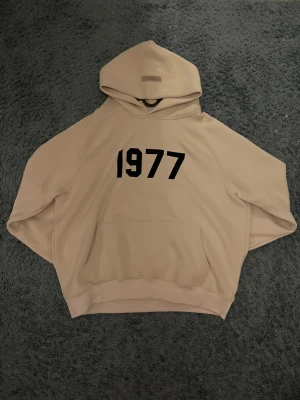 Essentials hoodie - Snygg beige hoodie från Essentials i storlek M med svart 1977-tryck på bröstet. Hög kvalitativ och sitter möjligtvis lite ”baggy”. Ej ”autentisk”. Oanvänd och pris kan diskuteras. 