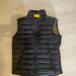 Svart dunväst från Parajumpers - Äkta väst köpt från Parajumpers egna hemsida, Snygg svart dunväst från Parajumpers med quiltad design och gul detalj vid kragen. Västen har två dragkedjeförsedda fickor och hög krage. Perfekt att slänga över en hoodie eller tröja när det är kyligt ute. Storlek Y/L passar perfekt på mig och jag är cirka 180cm 63kg.
