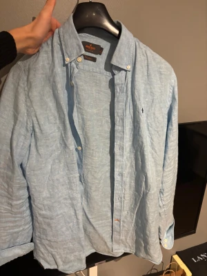 Ljusblå linneskjorta från Morris - Säljer en ljusblå skjorta från Morris i 100% linne. Skjortan har klassisk krage med knappar, lång ärm och diskret logga broderad på bröstet. 