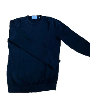 Svart tröja från Bläck - En stilren svart stickad tröja från bläck med rund halsringning och långa ärmar. Tröjan har en klassisk passform och är perfekt för lager-på-lager. Enkel och clean design som funkar till allt.