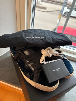 Saint laurent  - Säljer ett par sällsynta Saint Laurent sneakers i mörkblå sammet med svarta stjärnor och svarta snören. Skorna har vit platt sula och kommer med originalförpackning, extra vita skosnören och dustbag. Perfekt för dig som vill sticka ut med designerstil!