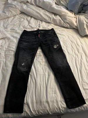 Svarta jeans från Dsquared2, strl 40 - Säljer ett par svarta jeans från Dsquared2 i storlek 40. Knappt använda.De har slitna detaljer och snygga tvättade effekter på både fram- och baksidan. Klassisk femficksmodell med smal passform och låg midja. Perfekt för dig som gillar märkes kläder 