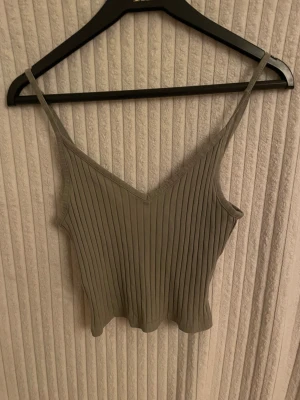Grön ribbad linnetopp med v-ringning - Säljer en stilren beige linnetopp med smala axelband och v-ringad hals. Toppen har ett ribbat mönster och är i bra skick, säljs i befintligt skick. 