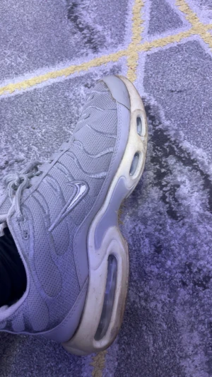 Nike Air Max Plus Tn sneakers grå - Nike Air Max Plus Tn sneakers i grått med mesh och syntetpaneler, ikonisk Tn Air-logga på hälen och synliga luftkuddar i sulan. Snygg vågig design på ovandelen, snörning och platt sula. Perfekt för dig som gillar streetwear och klassiska Nike-modeller.