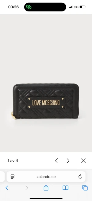 Svart quiltad plånbok Love Moschino - Snygg svart plånbok från Love Moschino med quiltad design och guldfärgade detaljer. Plånboken har ett stort fack med dragkedja och ett metallmärke med loggan framtill. Materialet är skinnimitation och insidan har flera fack för kort och mynt.