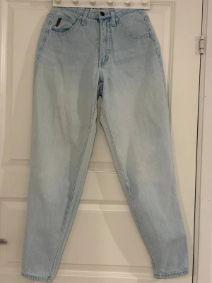 Ljusblå mom jeans från Armani Jeans - Säljer ett par ljusblå mom jeans från Armani Jeans med klassisk femficksdesign och hög midja. Jeansen har en snygg vintage-look, detaljerad tygpatch bak och metallogo på bakfickan. Perfekta för en avslappnad och trendig stil. Uppskattad storlek W25/26 L32. Slitage finns, därav priset, se bilder. 