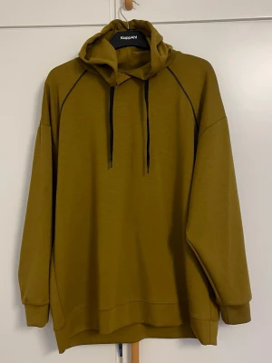 Olivgrön hoodie  - Olivgrön oversized hoodie  med svarta dragsnören och svarta detaljer längs axelsömmarna. Mjuk bomullsblandning, huva och ribbade muddar vid ärmslut och nederkant. Perfekt för en avslappnad och trendig stil.
