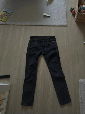 Svarta jeans från Replay - Säljer ett par svarta jeans från Replay med klassisk femficksdesign och dragkedja. Jeansen har en rak passform och är tillverkade i ett mjukt denimtyg som sitter snyggt. Perfekta för dig som gillar stilrena och tidlösa plagg.