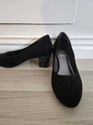 Svarta blockklack från Jana - Snygga svarta klackskor från Jana med rund tå och blockklack i ormskinnsmönstrat material. Skorna har en klassisk design i mockaliknande tyg och är perfekta för dig som vill ha både stil och komfort. Storlek 37H. Sällan andvända 