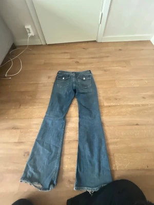 Blå bootcut  - Säljer ett par blå bootcut jeans med råa kanter nertill. Jeansen har klassisk femficksdesign och utsvängda ben. Perfekta för dig som gillar en avslappnad och trendig stil. Materialet är denim i bomull.