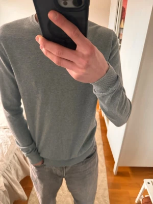 Ljusgrå basic tröja i bomull från Kappahl - En stilren ljusgrå tröja med rund halsringning och långa ärmar. Tröjan har ribbade muddar vid ärmslut och nederkant, vilket ger en clean och enkel look. Perfekt att matcha med jeans eller andra basplagg. Materialet känns mjukt och bekvämt. Storlek S