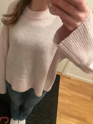 Ljusrosa stickad tröja med vida ärmar Gina tricot - Mysig ljusrosa stickad tröja med bred ribbad mudd vid hals, ärmslut och nederkant. Tröjan har en avslappnad passform och vida ärmar som ger en trendig look. Perfekt att matcha med jeans för en chill stil.