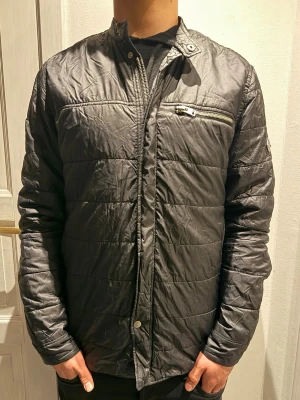 J.Lindeberg jacka  - Snygg svart J.Lindeberg jacka med ståkrage och dragkedja framtill. Jackan har en bröstficka med dragkedja och diskret logga på ärmen. Perfekt för dig som gillar stilren och enkel design.