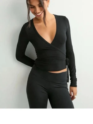 Svart omlott loungewear-set - Snyggt svart loungewear-set med omlottopp och långa ärmar. Toppen har djup v-ringning och knyt i sidan, byxorna är höga i midjan och sitter tight. Perfekt för chill dagar hemma eller när du vill vara bekväm men ändå se stylad ut.