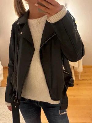 Svart skinnjacka från Missguided - Snygg svart skinnjacka från Missguided med klassisk bikerstil, silvriga dragkedjor och breda slag. Perfekt att slänga över en stickad tröja för en cool look. Jackan har detaljerade sömmar och flera fickor med dragkedja.