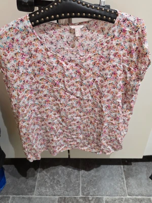 Blommig topp från Esprit - Söt blommig topp från Esprit med korta ärmar och rund halsringning. Toppen har ett färgglatt mönster i rosa, blått, gult och svart på vit botten. Perfekt för dig som gillar en avslappnad och feminin stil.