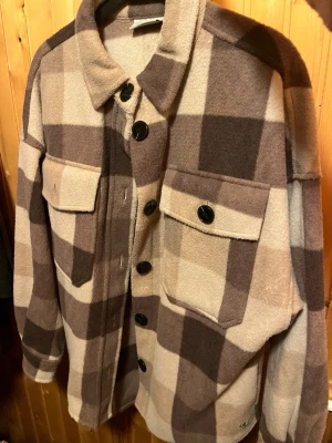 Rutig kappa - Oversized kappa i mjukt, tjockt material från Zink med stora rutiga mönster i beige, brunt och creme. Klassisk krage, svarta knappar framtill och två bröstfickor.