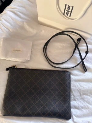 Svart axelväska från By Malene Birger - Snygg svart axelväska från By Malene Birger i läder med diskret rutmönster. Väskan har en avtagbar och justerbar axelrem samt guldfärgad dragkedja. Oanvänd dustbag och påse medföljer.