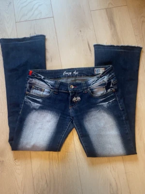 Crazy Age bootcut jeans - Säljer ett par coola blå bootcut jeans från Crazy Age. Jeansen har ljusa tvättade partier fram och bak samt drakmotiv på bakfickorna. Strlk 40 men passar S-M
