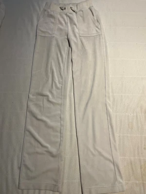 Beige mjukisbyxor med raka ben - Säljer ett par beige mjukisbyxor i mjukt velourmaterial. Byxorna har raka ben, bred resår i midjan med dragsko och stora fickor fram samt bakfickor med knappdetaljer. Perfekta för chill dagar och riktigt sköna att ha på sig.