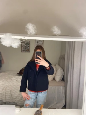 Mörkblå kort rock med krage - Snygg mörkblå rock med dubbelknäppning och bred krage. Modellen är kortare och har en klassisk, stilren look. Perfekt att slänga över en hoodie eller tröja för en cool vardagsstil.