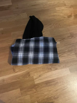 Rutig overshirt med svart luva - Snygg overshirt i svartvitt rutigt mönster med knappstängning framtill och en svart huva i sweatshirtmaterial. Perfekt för lager på lager och ger en avslappnad streetwear-look. Långa ärmar och mjukt tyg för extra komfort.