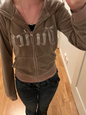 Biege hoodie från Juicy Couture - Säljer en biege juicy couture tröja med diamant text på bröstet, lite sliten i armarna och  dragkedjan. Nypris 900kr. 