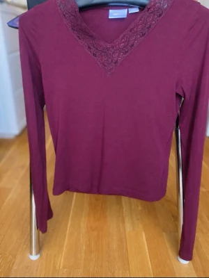 Vinröd långärmad topp Gina Tricot - Snygg vinröd långärmad topp från Gina Tricot med spetsdetaljer runt v-ringningen. Tillverkad i mjukt material som sitter skönt på kroppen. Perfekt för dig som vill ha en enkel men ändå elegant look.
