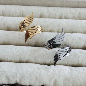 Ringar med vinge-design  - Säljer coola ringar i form av vingar, finns i både guld- och silverfärgad. De har en öppen design som ger en edgy och unik look. Perfekt accessoar för dig som vill sticka ut med detaljerade smycken.