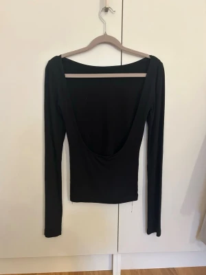 Svart långärmad topp med öppen rygg - Trendig svart långärmad topp med djup, öppen rygg och tight passform. Perfekt för dig som vill ha en enkel men ändå statement topp. Tillverkad i mjukt stretchigt material som sitter snyggt på kroppen. Soft touch material