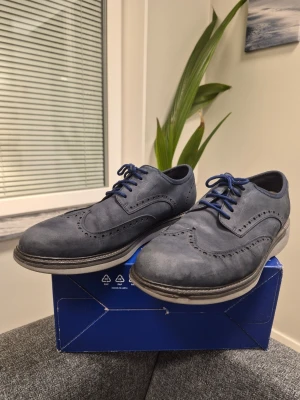 Cole Haan Grand Wingtip Oxford mörkblå skor EUR 44.5 US 10.5 - Snygga mörkblå loafers med klassiskt broguemönster och blå snören. Skorna har en låg profil och är tillverkade i mockaliknande material med ljusgrå sula. Perfekta för dig som vill ha en stilren och modern look.