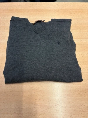 Morris V-Ringad tröja  - Mörkgrå stickad tröja med V-ringning och diskret broderad logga på bröstet. Tröjan har långa ärmar och ribbade muddar vid ärmslut och nederkant. Perfekt för lager-på-lager och enkel att matcha med jeans eller chinos. Tröjan är i storlek S men det är slim fit passform på den så passar även XS.