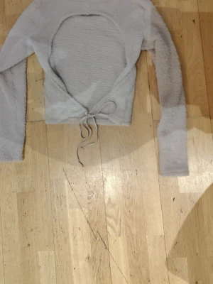 Ljusgrå fluffig stickad tröja - Mysig ljusgrå stickad tröja med fluffig textur och långa ärmar. Tröjan har rund halsringning och en dragsko i midjan för justerbar passform. Perfekt för lager på lager och chill dagar.