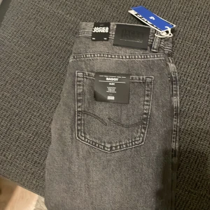 Ett par helt nya Baggy grå jeans från Jack & Jones - Säljer ett par gråa baggy jeans från Jack & Jones, modell Alex. Jeansen har en avslappnad passform, klassisk femficksdesign och är tillverkade i slitstarkt denim. Perfekt för dig som gillar en loose och trendig stil.