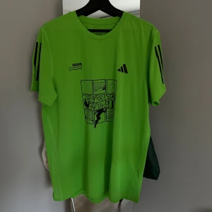 Adidas Stockholm Halvmarathon 2024 Finisher T-shirt – Herr - Säljer en helt oanvänd grön Adidas t-shirt med svart tryck från Stockholm Halvmarathon 2024. T-shirten har korta ärmar, svart Adidas-logga och coolt grafiskt motiv på bröstet. Materialet är lätt och andas, perfekt för träning eller löpning.